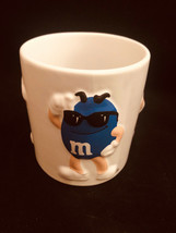 M&Ms purple mug with yellow M&M wearing a blue hat woth purple  string tie.